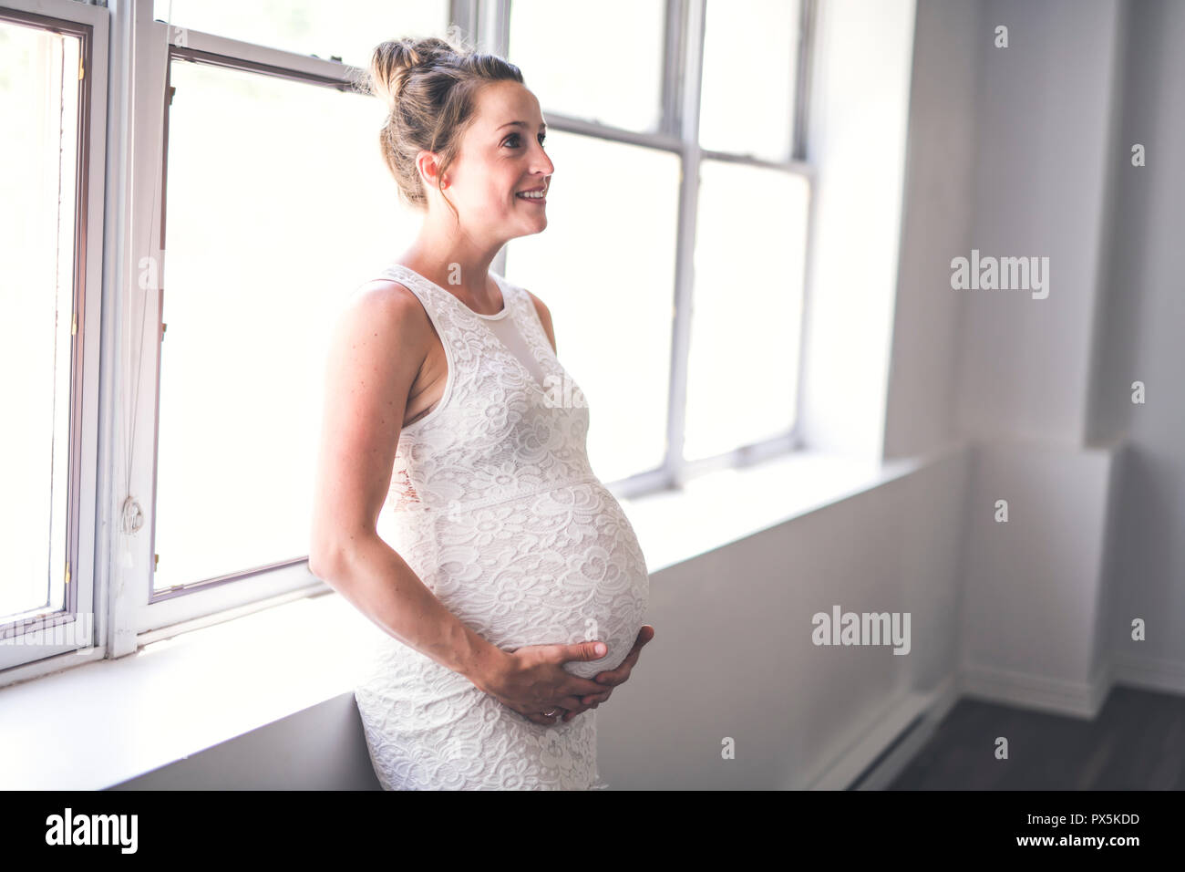 Une femme enceinte avec le ventre à la maison près d'une fenêtre Banque D'Images