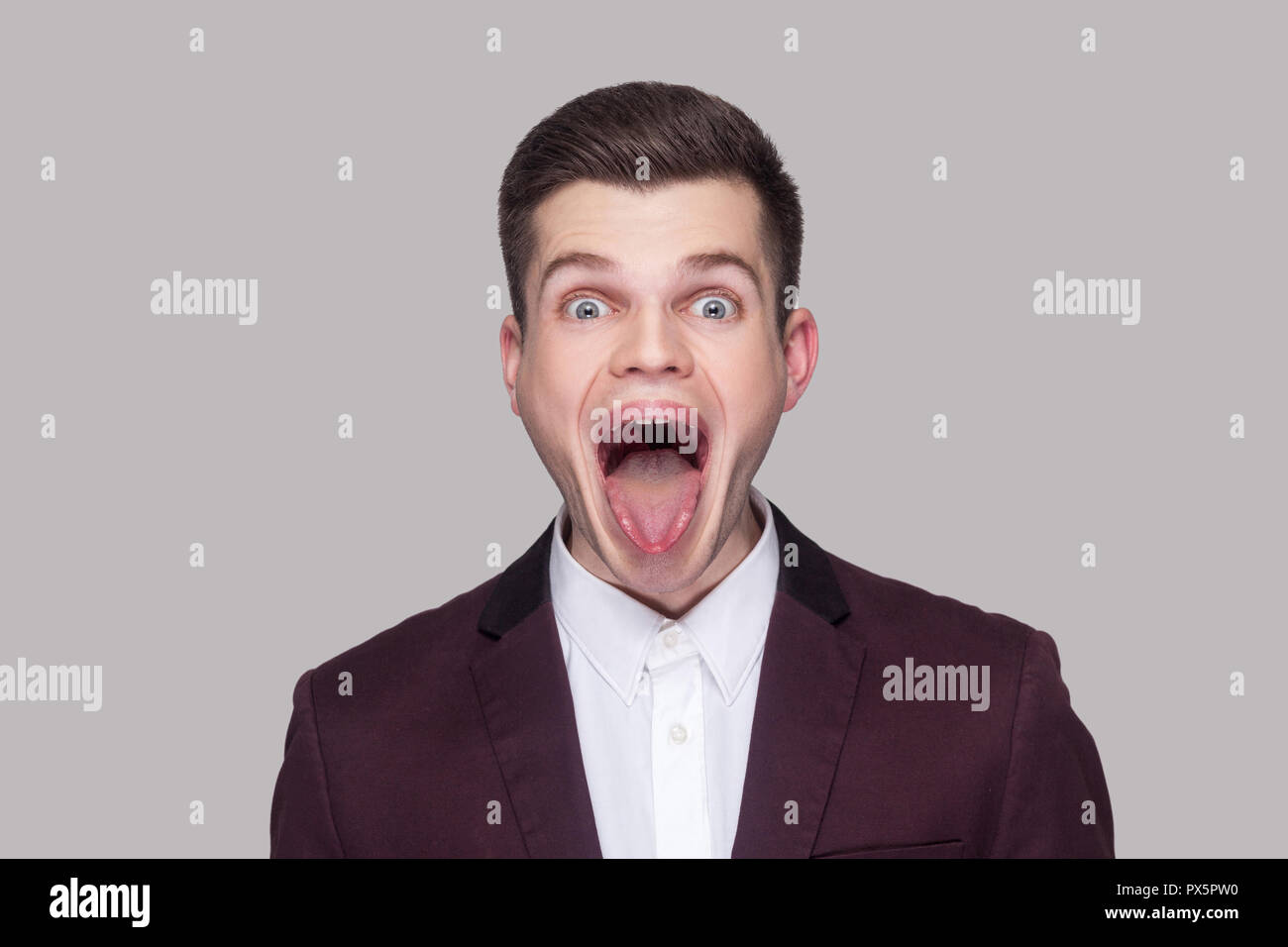 Portrait de funny crazy beau jeune homme en costume violet et chemise blanche, debout, avec la bouche ouverte, langue, et de grands yeux. indoo Banque D'Images Portrait de funny crazy beau jeune homme en costume violet et chemise blanche, debout, avec la bouche ouverte, langue, et de grands yeux. indoo Banque D'Images