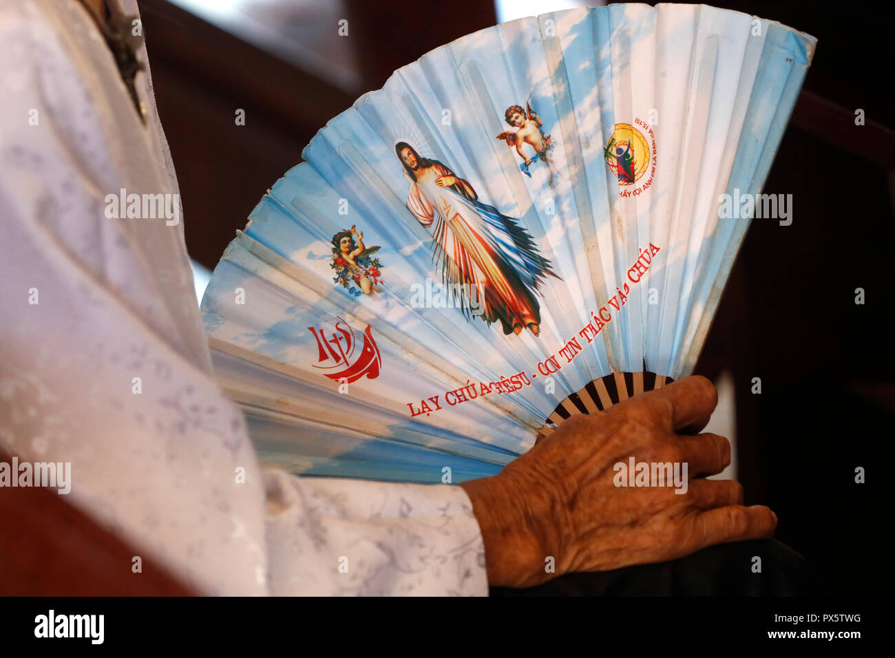 Hai fils église catholique. Vieille Femme tenant Jésus Miséricordieux ventilateur. Ba Ria. Le Vietnam. Banque D'Images