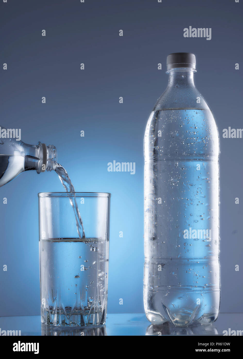 Verser de l'eau de la bouteille en verre sur fond bleu Banque D'Images