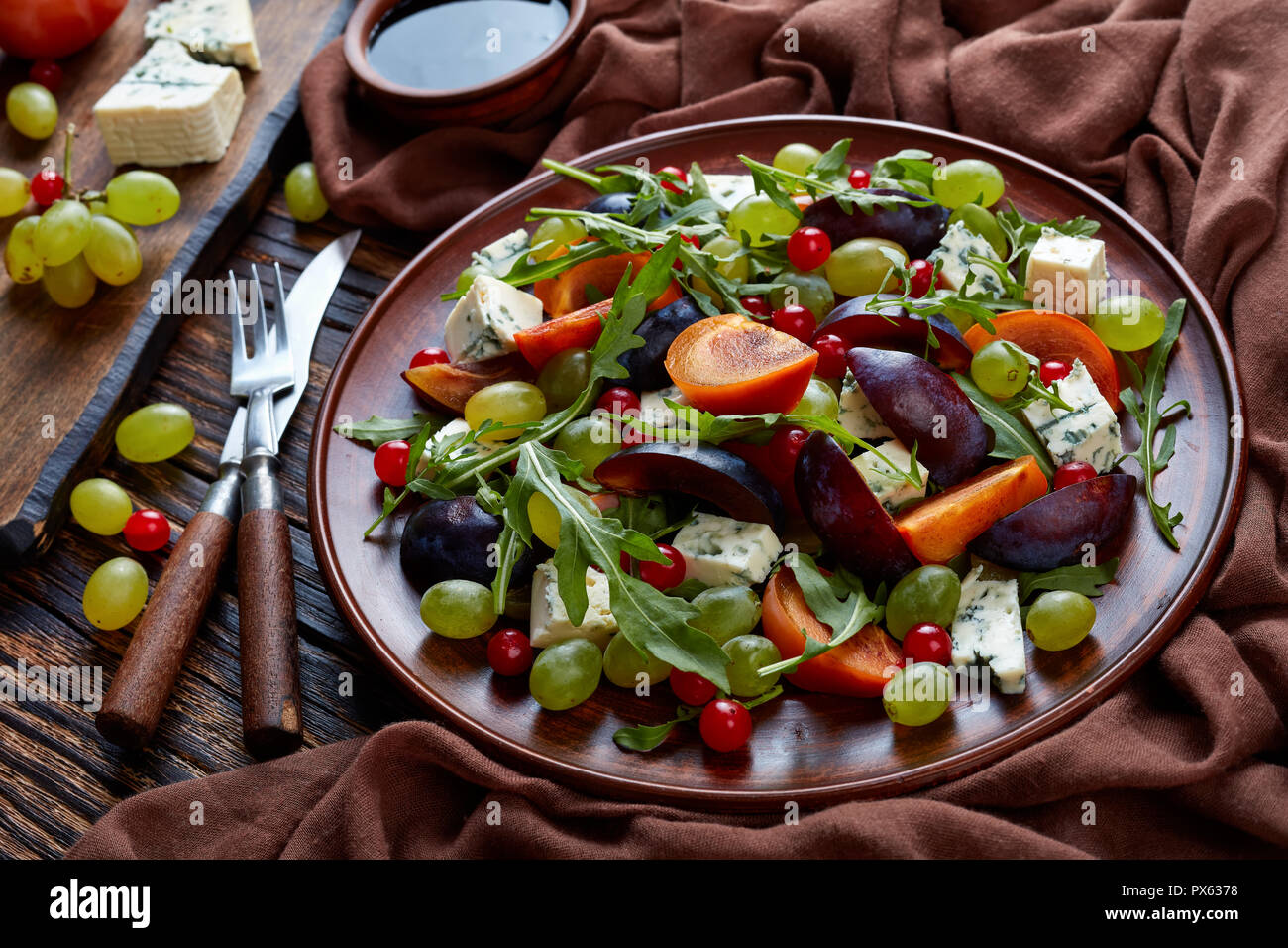 Close-up d'automne délicieux chocolat salade de kaki, fromage bleu, raisin vert, tranches de prune et la roquette sur une plaque de faïence avec ingrédient actif Banque D'Images