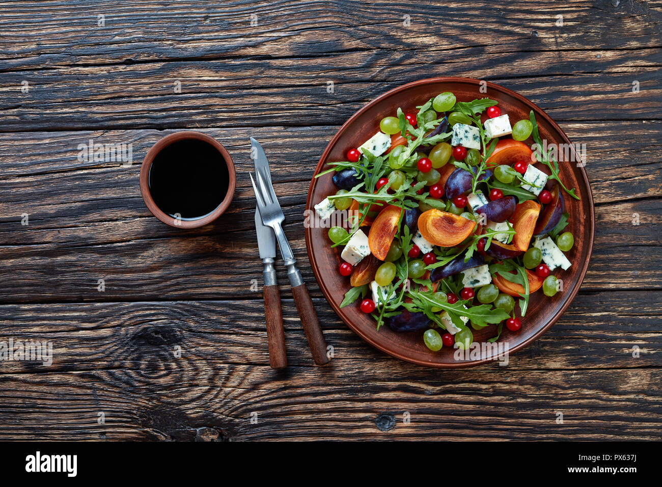 Vue supérieure de l'automne délicieux chocolat salade de kaki, moisissure bleue fromage, raisins verts, de prune et de tranches de roquette sur une plaque de faïence sur un Banque D'Images