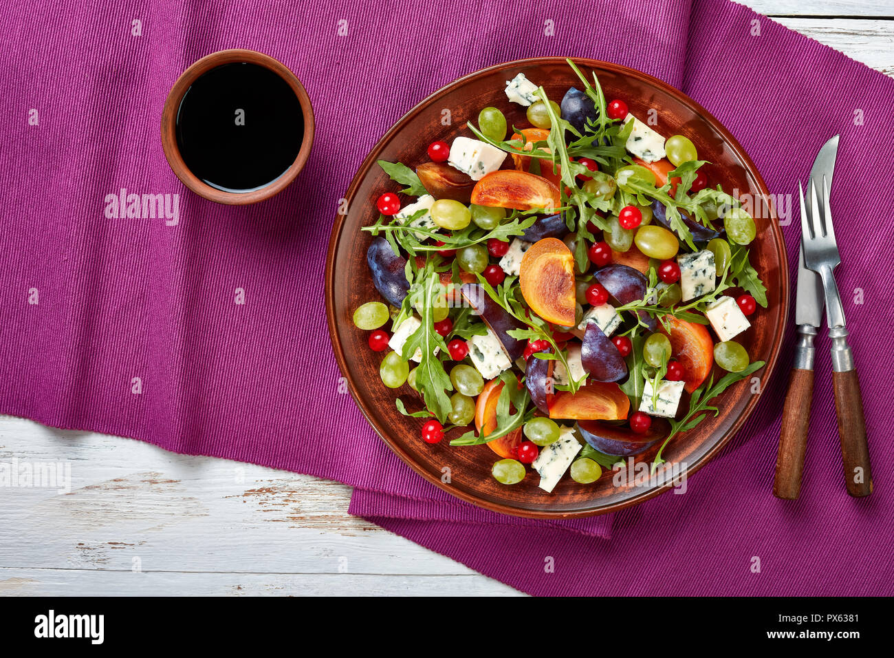 Vue supérieure de l'automne sain avec salade de kaki, chocolat, fromage moule bleu raisin vert, prune et la roquette sur une plaque d'argile avec du vinaigre sucré dr Banque D'Images