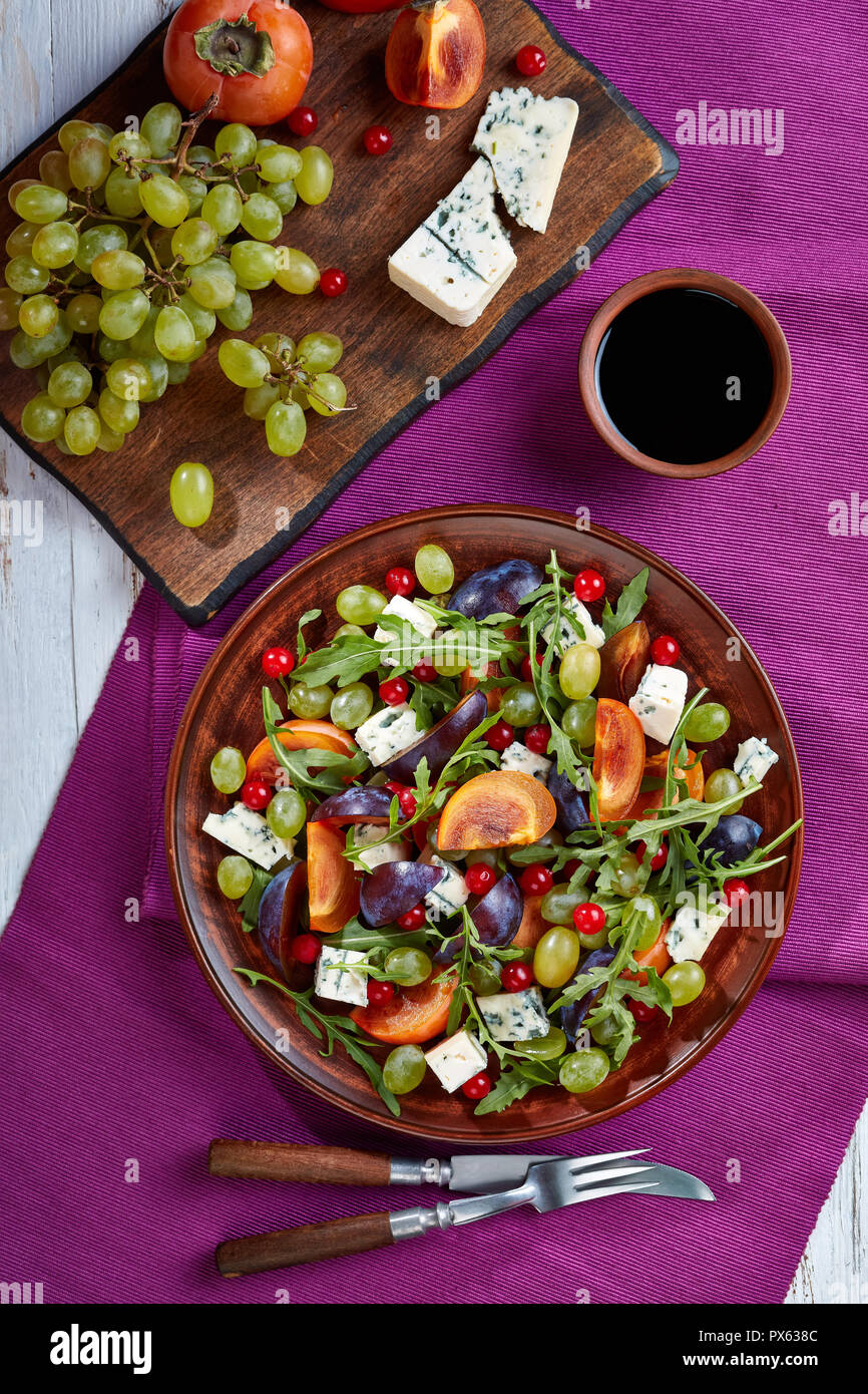 Salade d'automne sain avec kaki, chocolat, fromage moule bleu raisin vert, prune et la roquette sur une plaque d'argile avec vinaigre sucré, vertical Banque D'Images