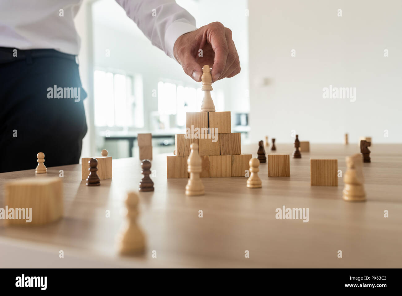 Hiérarchie d'affaires de concept d'échecs plaçant la figure du roi au-dessus de blocs de bois empilées en bois et d'autres chiffres répartis sur l'office des Banque D'Images