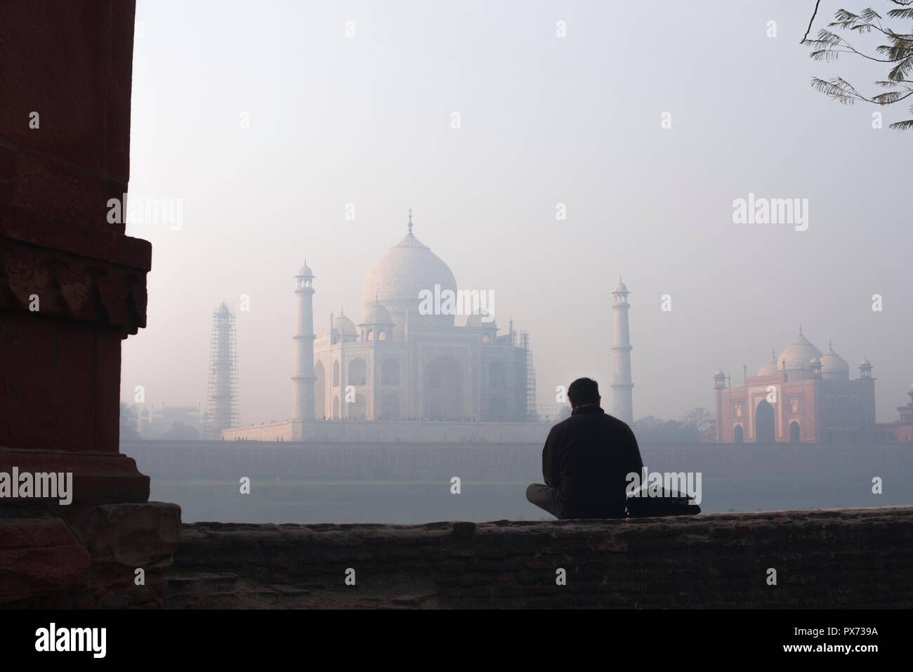 Taj Mahal la merveille du monde et la fierté de l'Inde en hiver doux matin lumière chaude avec haze et surveillé par un homme assis en face de tourisme Banque D'Images