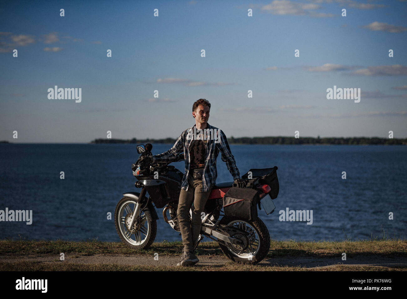 Beau biker, debout près de sa moto au bord du lac Banque D'Images