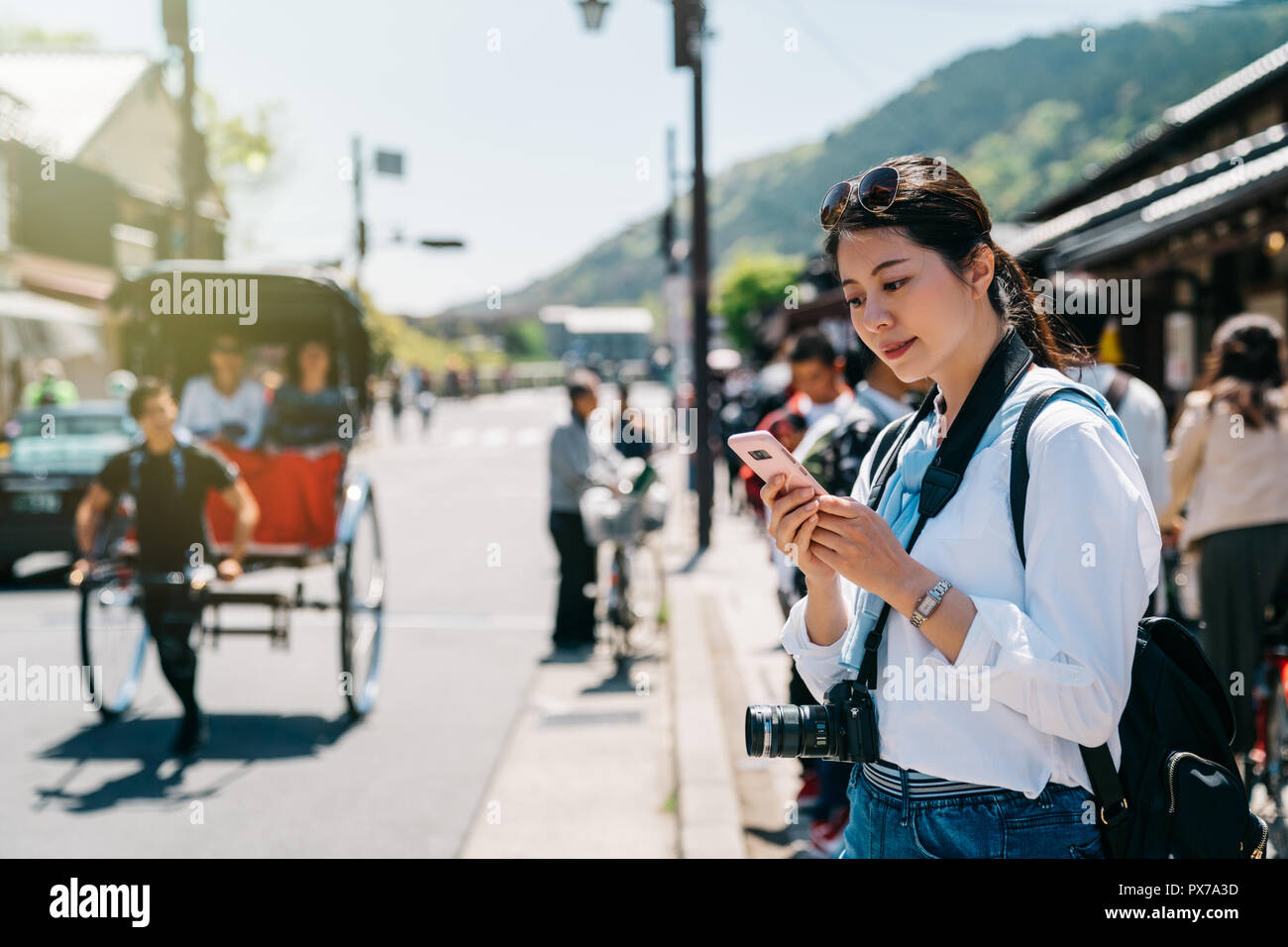 Photographe fille élégante debout sur la route et à l'aide d'un téléphone cellulaire tout en rickshasw tiré quelques passé. foule marche sur la grouillante rue. Charmantes Hôtesses Japonaises Banque D'Images