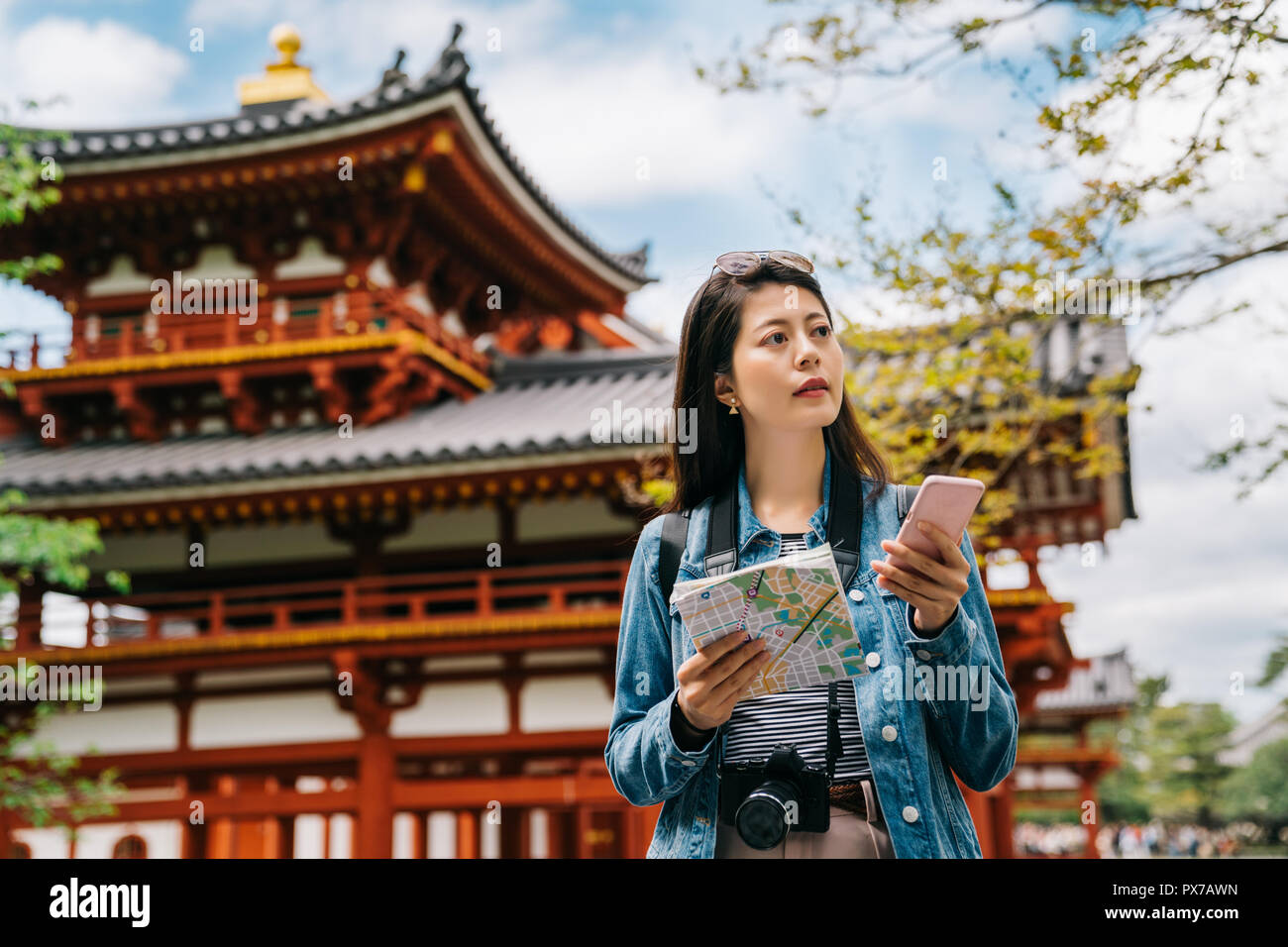 Asian tourist en utilisant smartphone et la carte pour rechercher le prochain endroit à visiter dans temple Byodo sur l'arrière-plan avec ciel bleu. billet lens homme chatti Banque D'Images