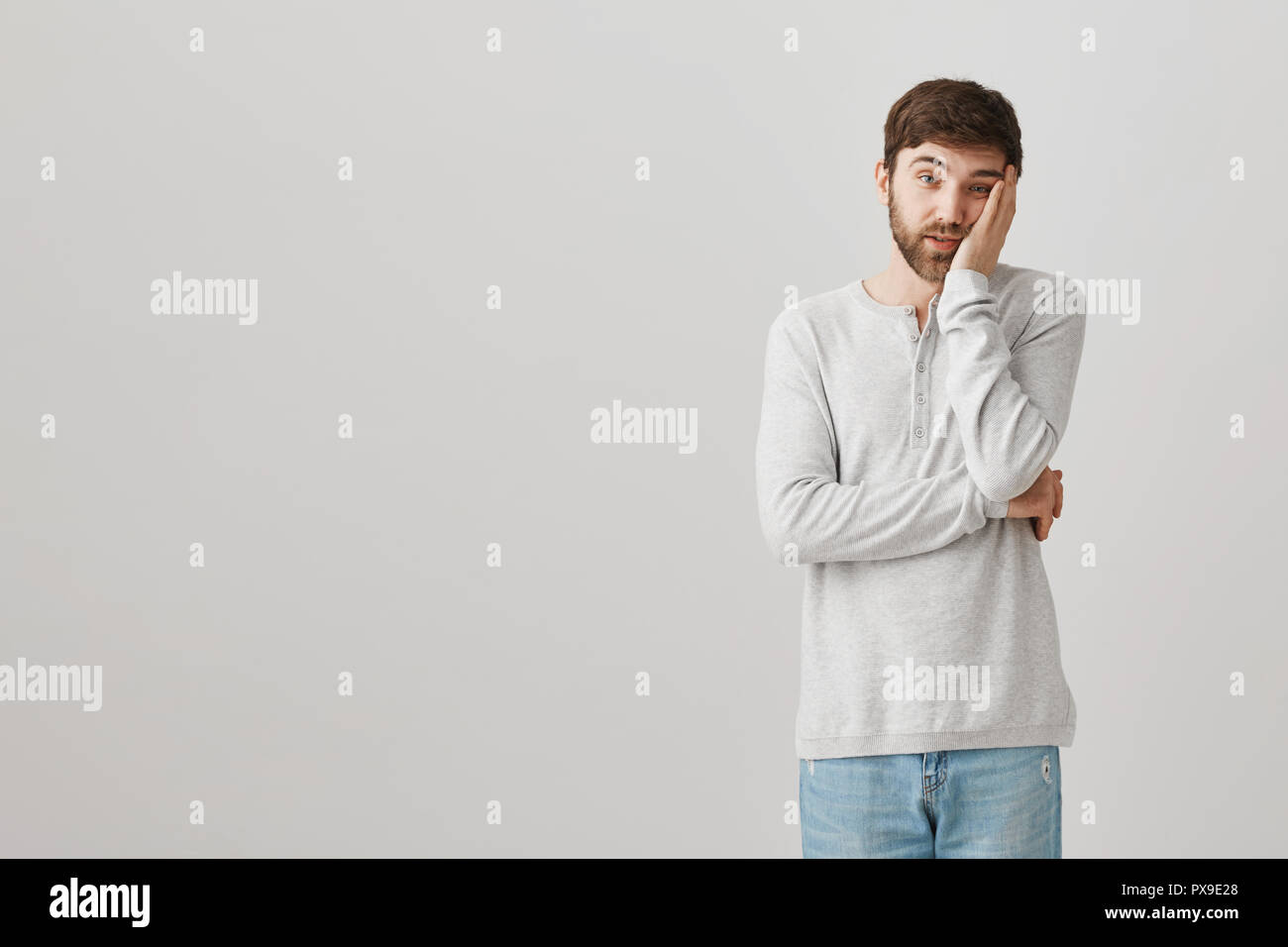 Tenir de temps dois-je écouter ce gars stupide. Portrait de l'ennui et stupéfié male student leaning head sur palm en étant debout sur fond gris, étant fatigué des discours politicien Banque D'Images
