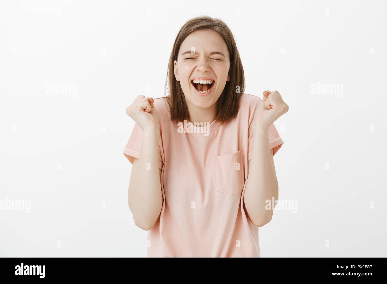 Oui J'ai gagné. Portrait de triomphant heureux et insouciant girl in pink t-shirt, criant avec large sourire et ferma les yeux de bonheur, gesticulant, poing levé célébrant la victoire ou la réussite Banque D'Images