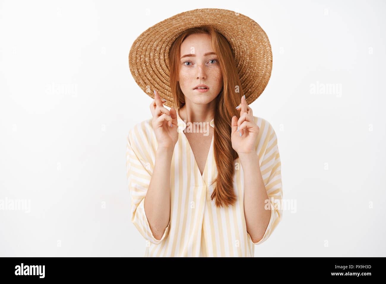 Bien concentré inquiète ginger girl with freckles en chapeau de paille d'été mignon Chemisier rayé et doigts de passage pour la bonne chance à concernés et inquiets en priant, ce souhait Banque D'Images