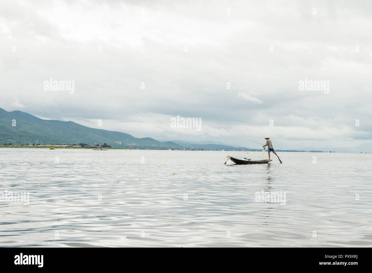 Transport local Les jeunes hommes portant des pêcheurs birmans, à l'aide de bâton et net pour le poisson, en équilibre sur un pied sur le bateau, le lac Inle au Myanmar, Birmanie Banque D'Images