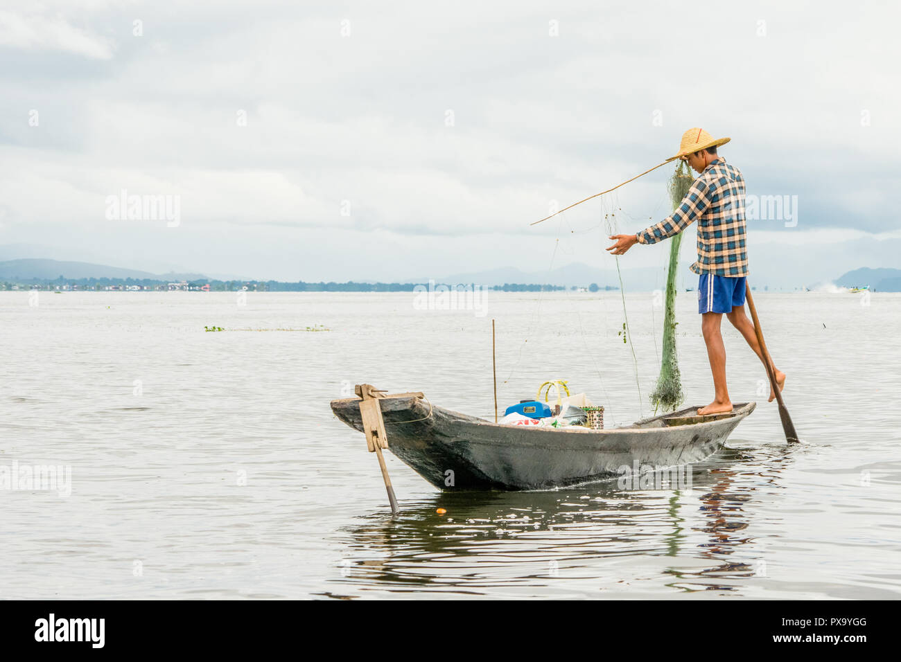 Transport local Les jeunes hommes portant des pêcheurs birmans, à l'aide de bâton et net pour le poisson, en équilibre sur un pied sur le bateau, le lac Inle au Myanmar, Birmanie Banque D'Images