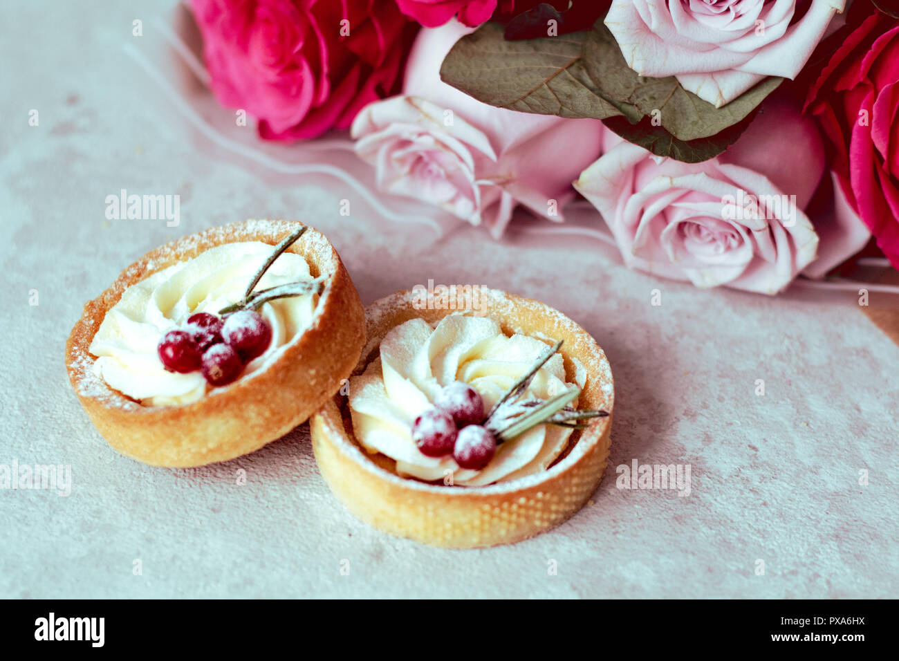 Offre cadeau romantique : des gâteaux sucrés avec de la crème et des petits fruits et un bouquet de roses roses sur fond clair Banque D'Images