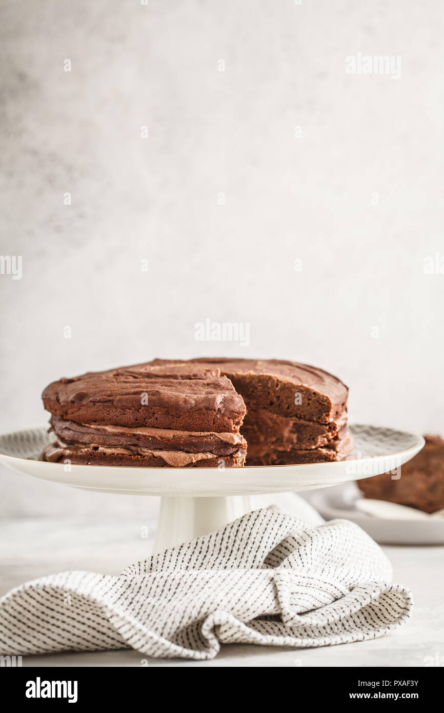 Gâteau au chocolat Végétalien sur un plat blanc pour gâteau, fond clair. La nourriture végétalienne saine concept. Banque D'Images