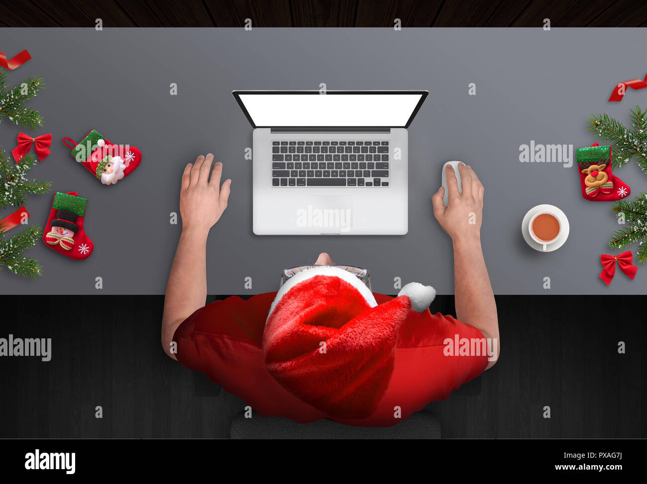 L'homme travaille dur sur l'ordinateur portable durant les vacances de Noël. Vue supérieure de la scène avec l'arbre de Noël et décorations. Guy with Santa Claus hat. Banque D'Images