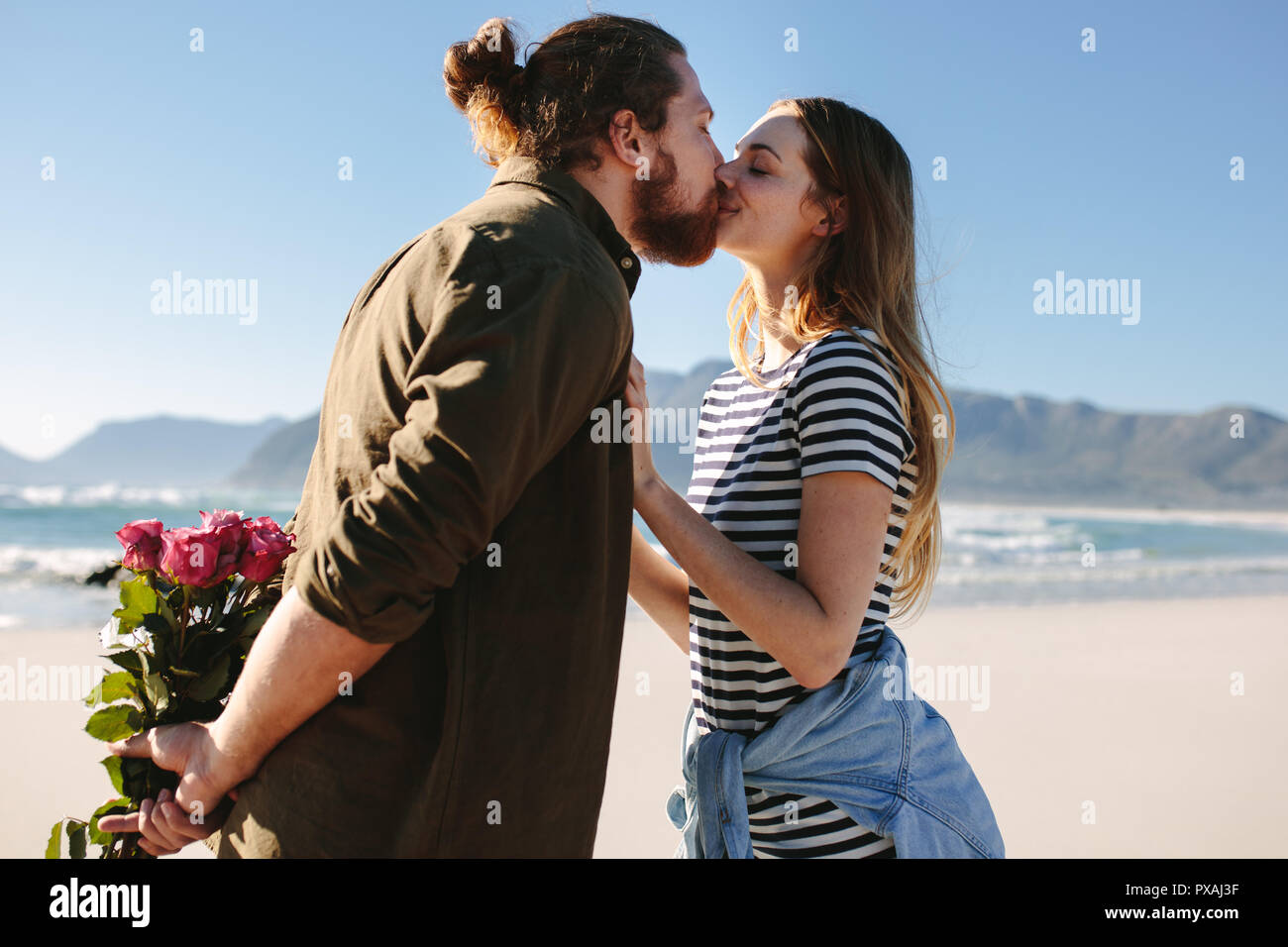 Man holding surprise bouquet de roses pour la belle jeune femme sur la plage. Couple amoureux, baiser sur la plage. Banque D'Images