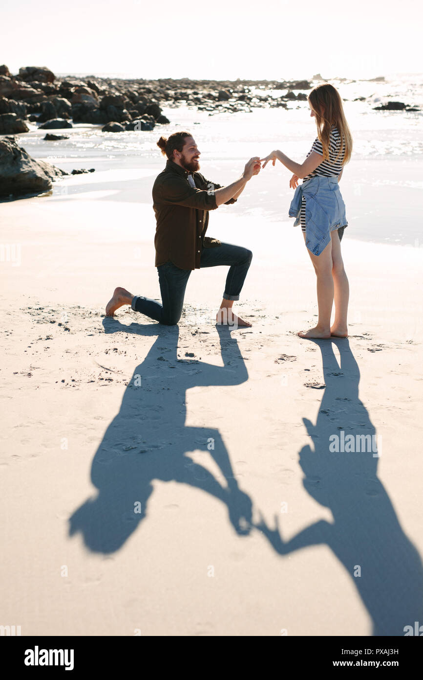 Qui fait semblant de mettre un anneau au doigt, petite amie de la mer. L'homme vers le bas sur un genou mettre une bague de fiançailles sur le doigt de petite amie à plage. L'homme pr Banque D'Images