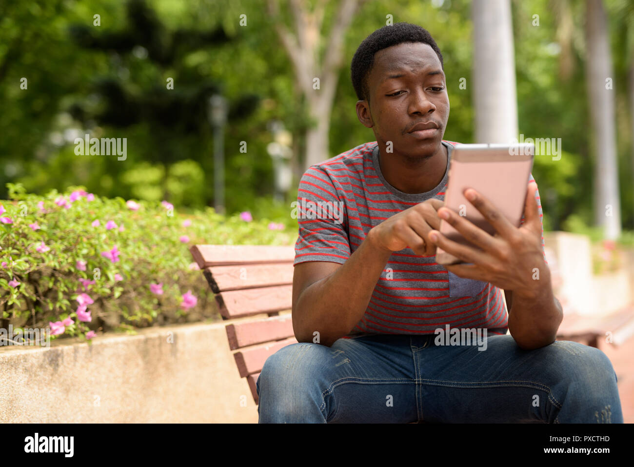 Beau jeune homme africain using digital tablet in park Banque D'Images