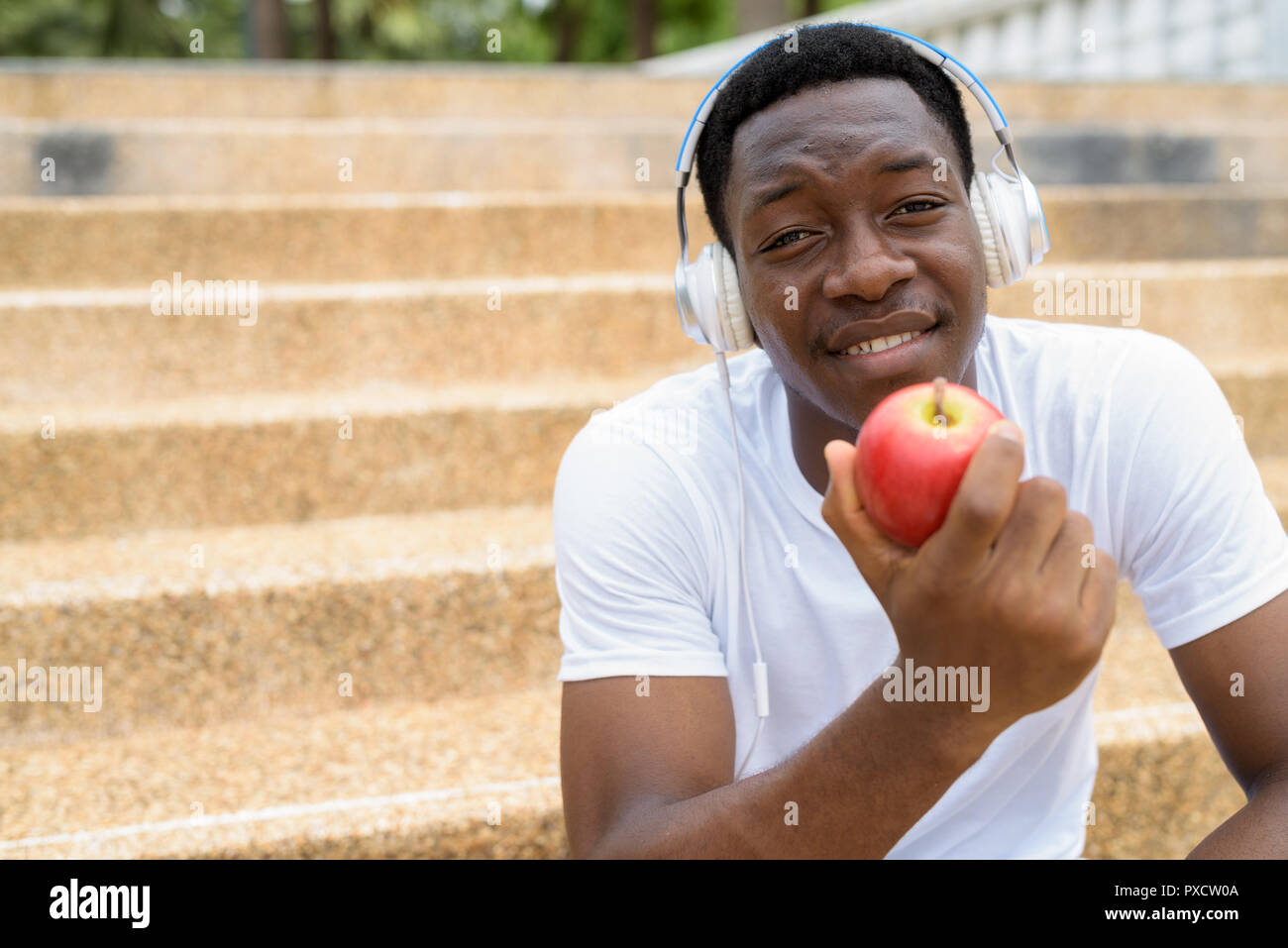 Homme africain à l'écoute de la musique avec des écouteurs et holding Red Apple Banque D'Images