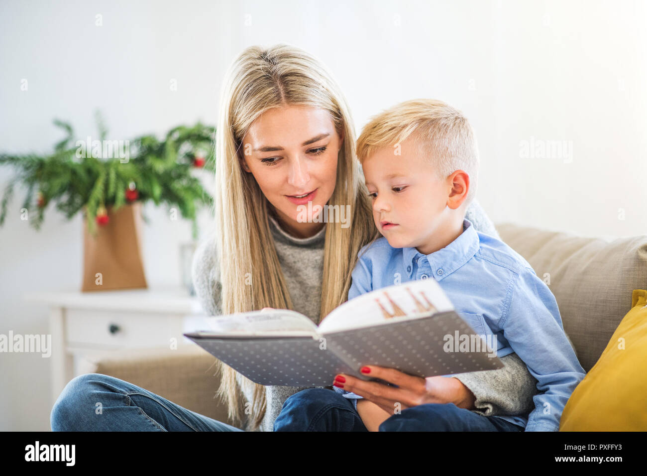 Une mère et petit garçon assis sur un canapé à la maison au moment de Noël, de lire une histoire à partir d'un livre. Banque D'Images
