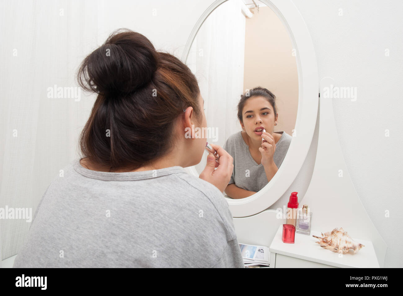 La jeune fille s'applique un miroir et regarde dans le miroir de coiffeuse Banque D'Images