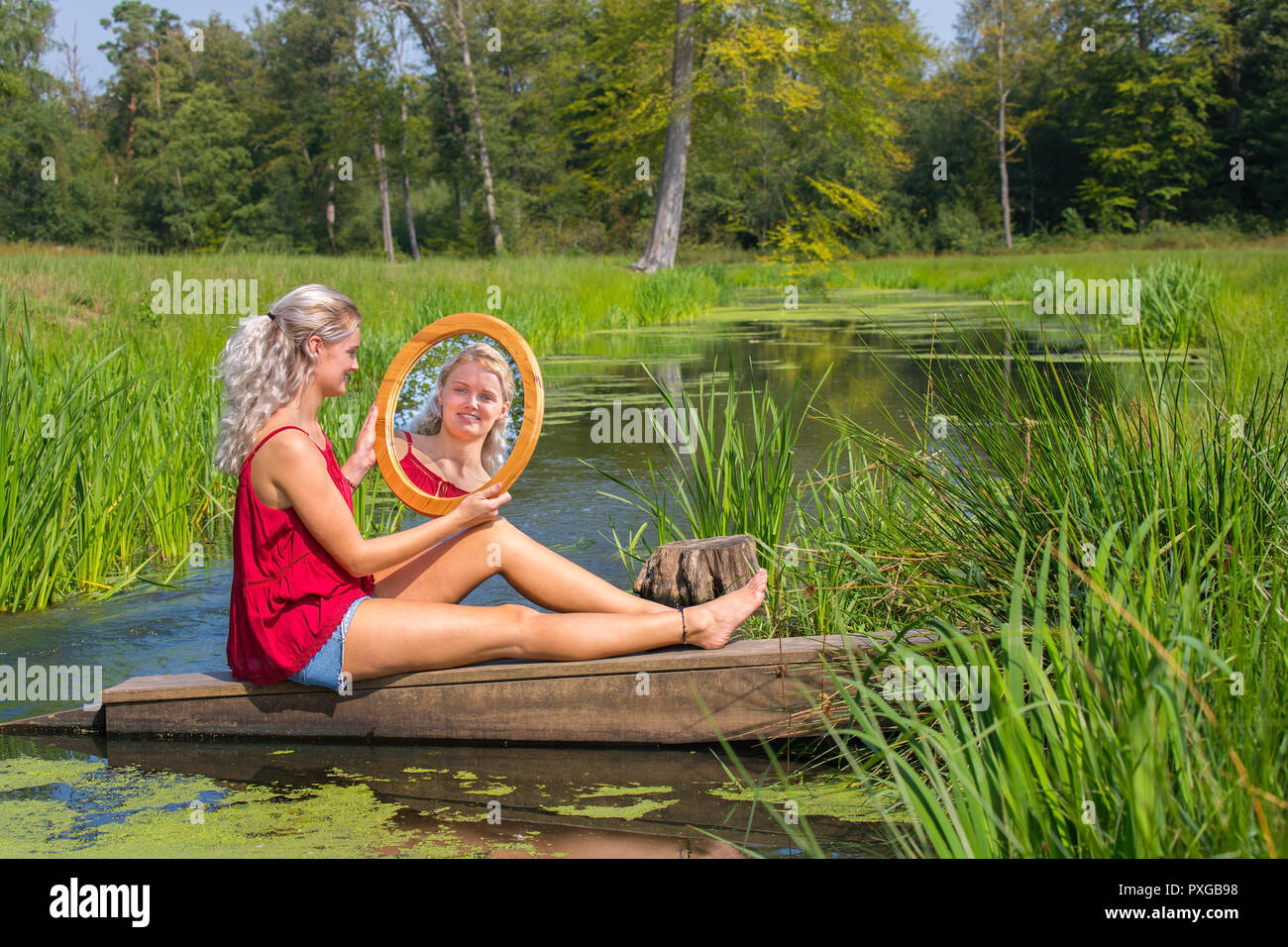 Jeune blonde hollandaise siège avec miroir à l'eau dans la nature Banque D'Images