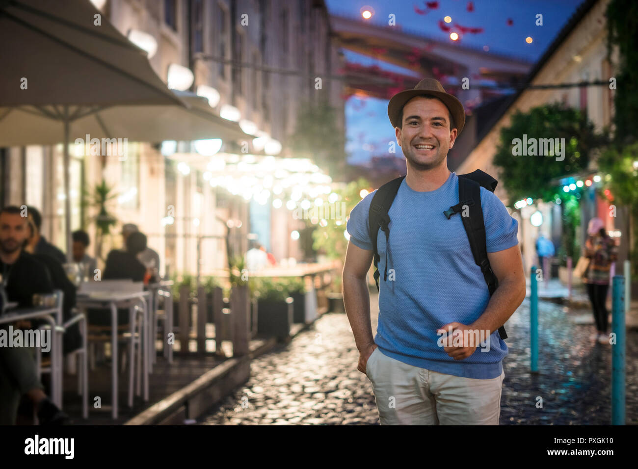 Heureux jeune homme en chemise bleue marche sur rues animées avec des restaurants à l'evevning Banque D'Images
