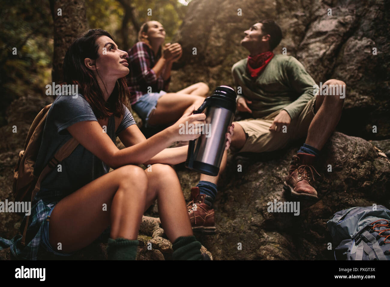 Femme assise sur des rochers holding thermos avec vos amis assis à l'arrière dans la forêt. Groupe d'amis en faisant une pause lors d'une randonnée dans la nature. Banque D'Images