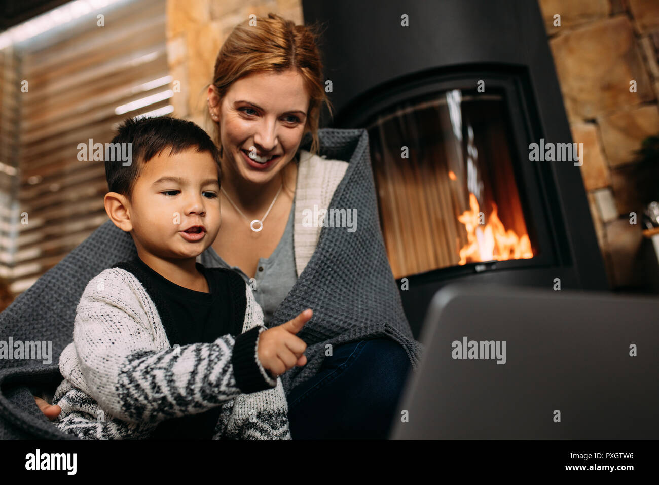 Little Boy pointing at laptop while sitting avec mère près de cheminée à la maison. La mère et le fils à la recherche de quelque chose d'intéressant sur l'ordinateur portable de Banque D'Images