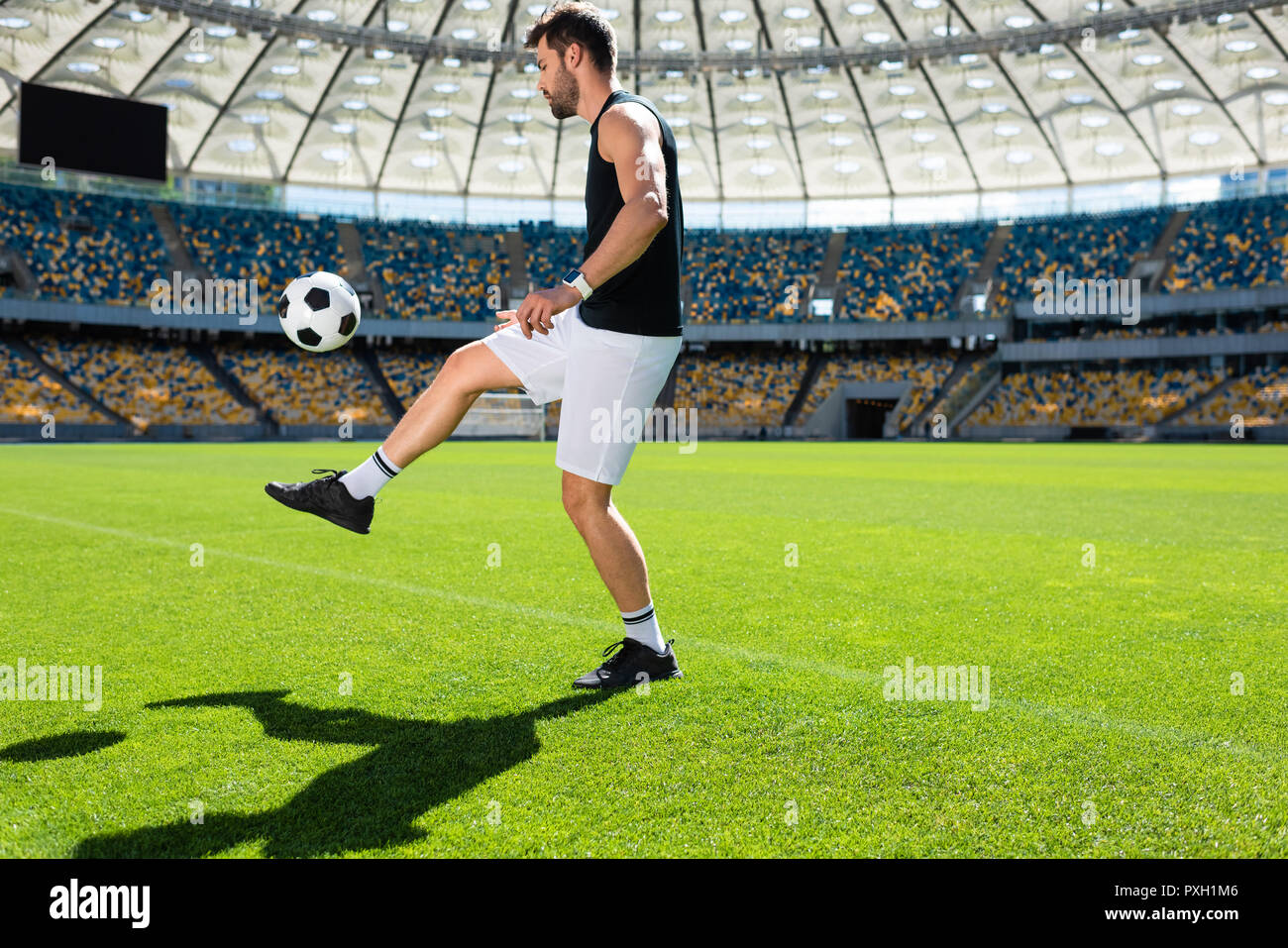 Jeune sportive joueur de foot balle rebondissante sur jambe à stade Banque D'Images