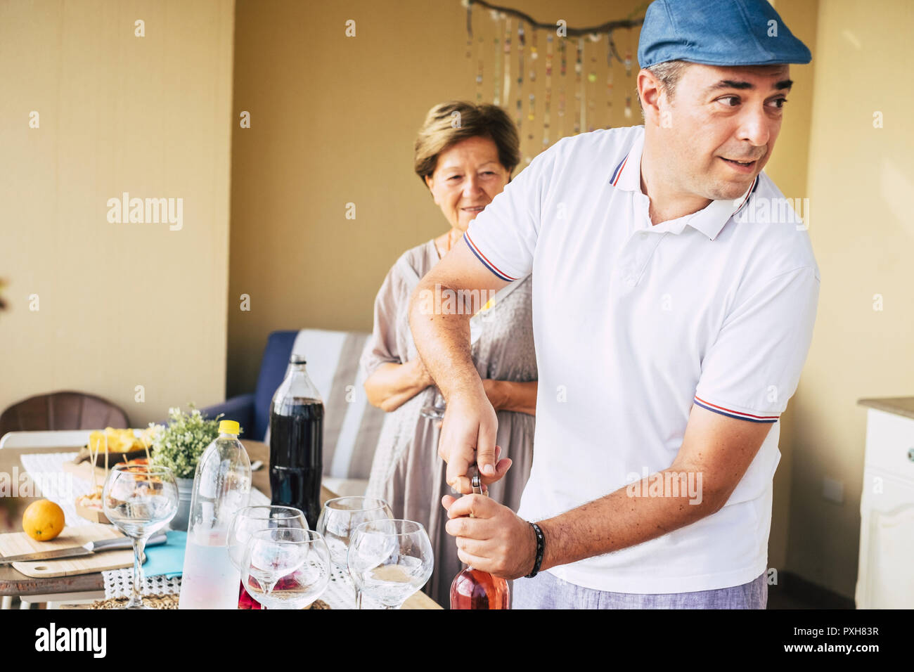 Homme d'âge moyen de l'ouverture d'une bouteille de vin rouge au cours d'un dîner de célébration avec des amis. Femme adultes âgés en contexte msile et attendre que le verre Banque D'Images