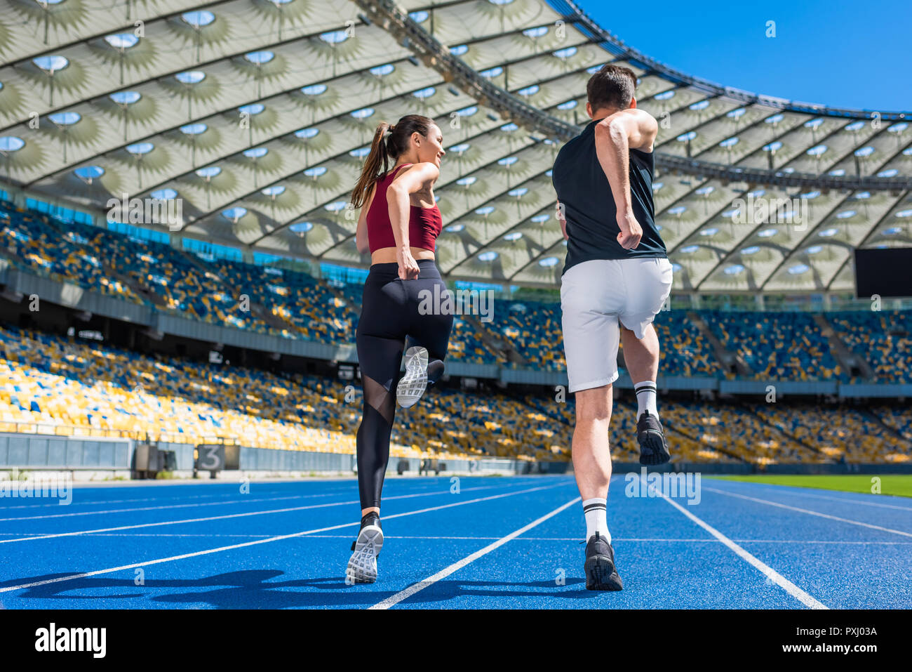 Vue arrière du jeune homme et femme joggers tournant sur la voie au stade de sport Banque D'Images