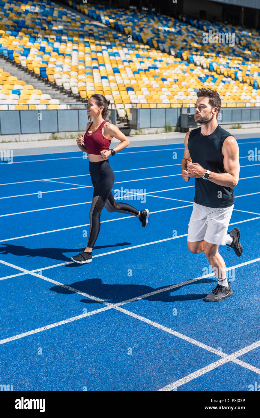 Séduisant jeune homme et femme joggers tournant sur la voie au stade de sport Banque D'Images