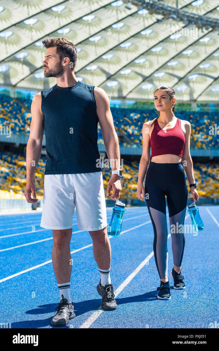 Jeune couple sportif avec des bouteilles d'eau de vous détendre sur une piste de course au stade de sport Banque D'Images