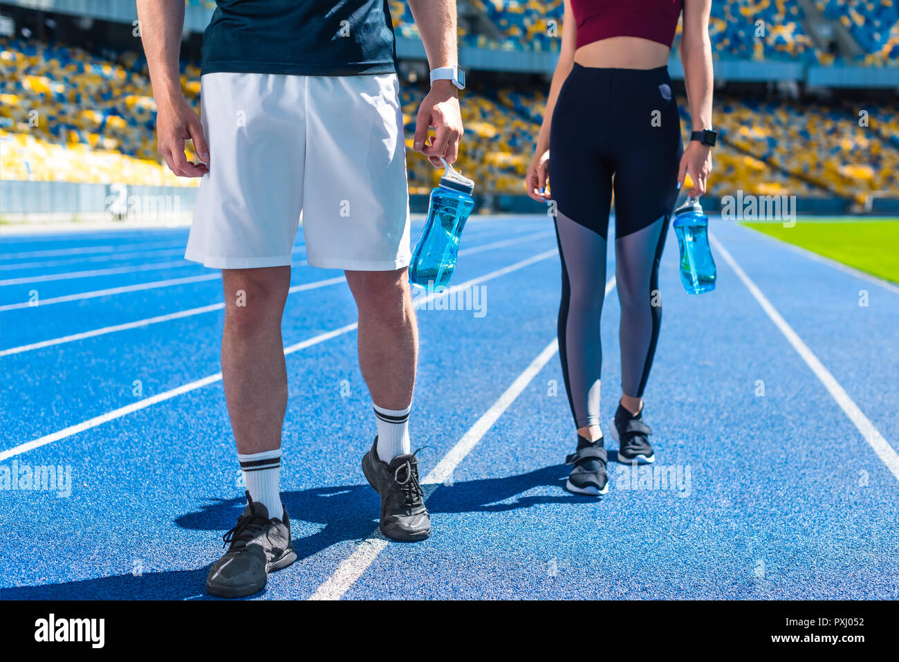 Cropped shot of couple sportif avec des bouteilles d'eau sur une piste de course au stade de sport Banque D'Images