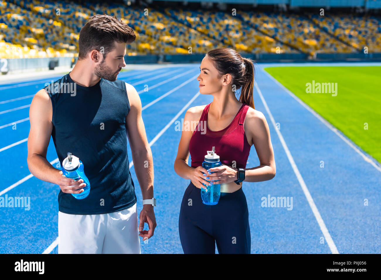 Jeune couple sportif avec des bouteilles d'eau sur une piste de course au stade de sport Banque D'Images
