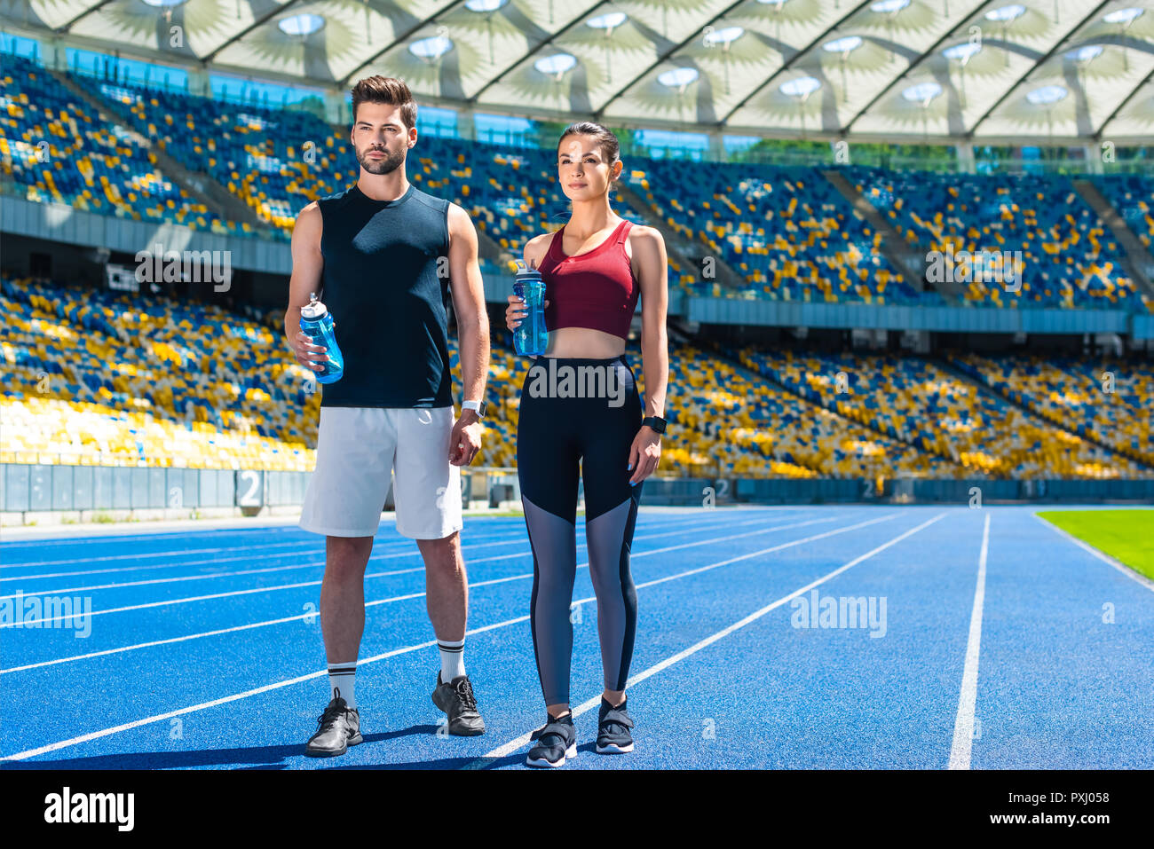 Jeune couple sportif avec des bouteilles d'eau de vous détendre sur une piste de course au stade de sport Banque D'Images