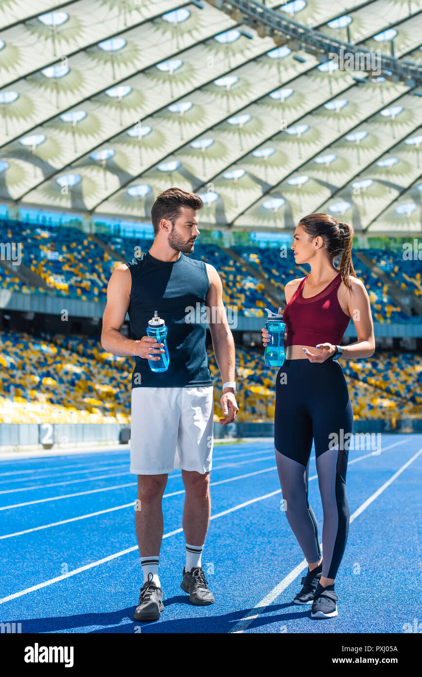 Jeune couple sportif avec des bouteilles d'eau debout sur une piste de course au palais des sports et de parler Banque D'Images