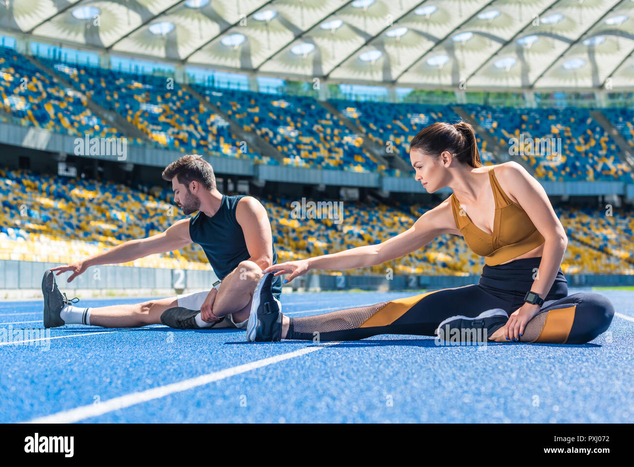 Les jeunes hommes et femmes d'athlétisme joggers assis sur une piste de course et de stretching chez sports stadium Banque D'Images