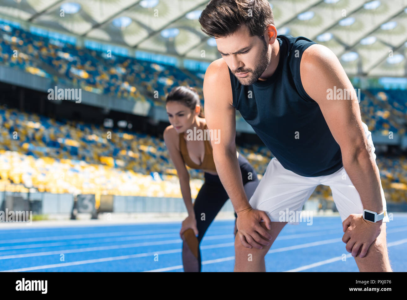Jeune couple fatigué debout sur une piste de course au stade après le jogging Banque D'Images