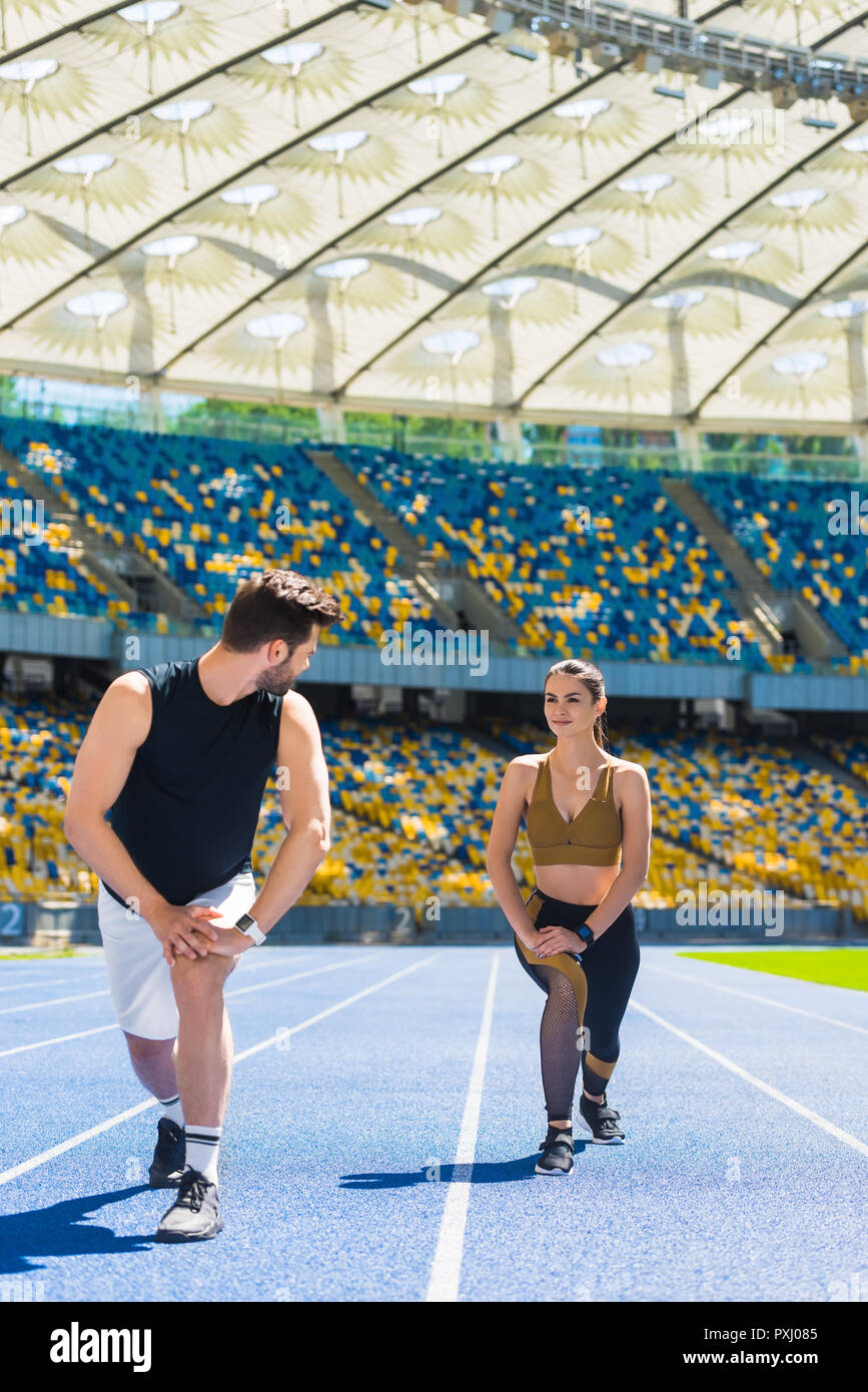 Jeune couple athlétique réchauffe les jambes avant la course sur une piste de course au stade de sport Banque D'Images