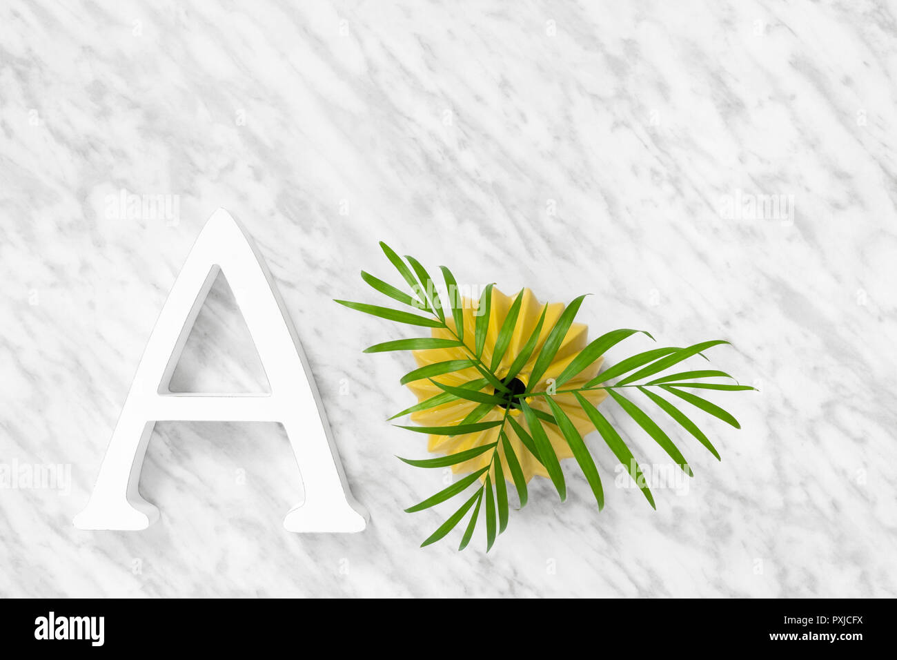 Une lettre et le vert des feuilles de palmier dans un vase en céramique jaune, sur fond de marbre. Banque D'Images