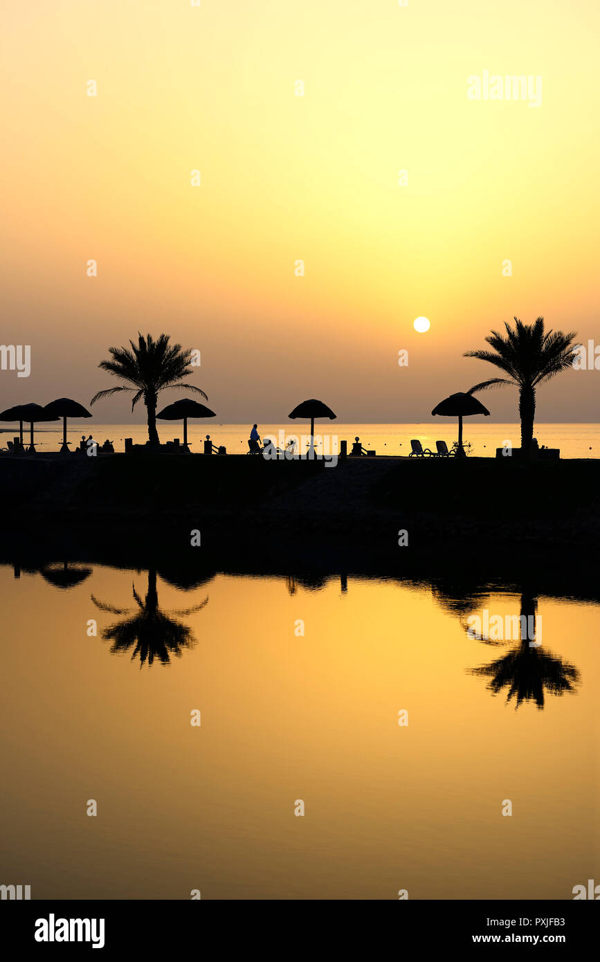 Coucher du soleil avec de l'eau la réflexion des palmiers et des parasols, l'hôtel Cove Rotana, Ras al Khaimah, Émirats Arabes Unis Banque D'Images