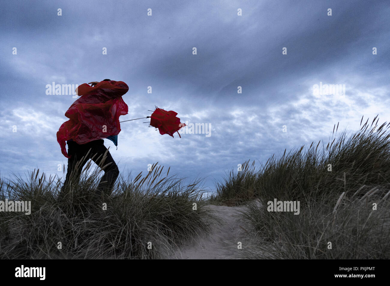 Homme portant un manteau de pluie imperméable rouge luttant avec un parapluie par temps venteux. Banque D'Images
