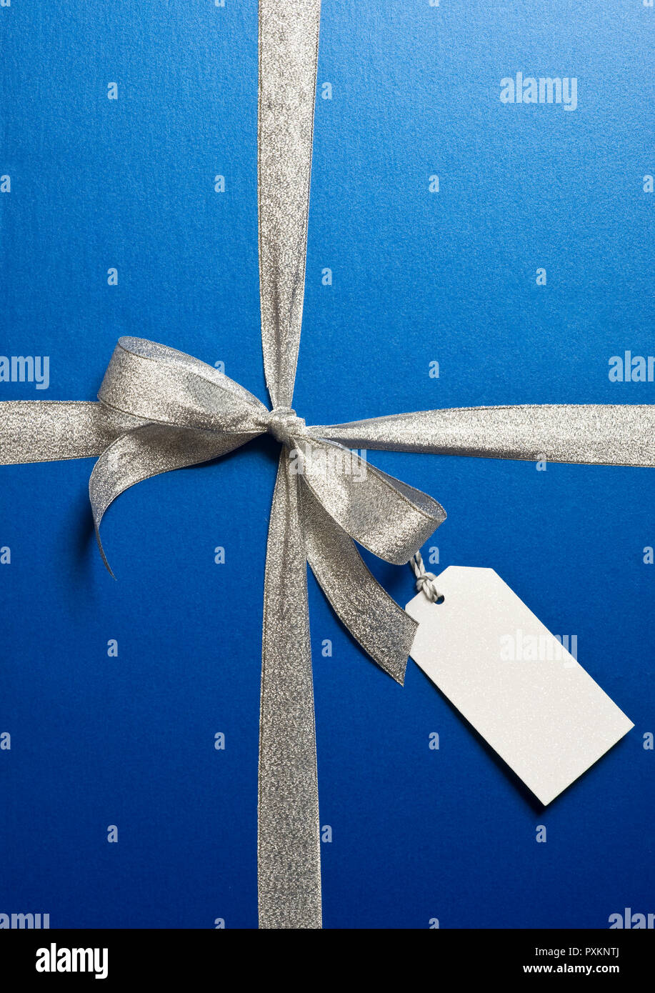 Un cadeau emballé dans du papier bleu et du ruban argent avec une étiquette cadeau blanche Banque D'Images
