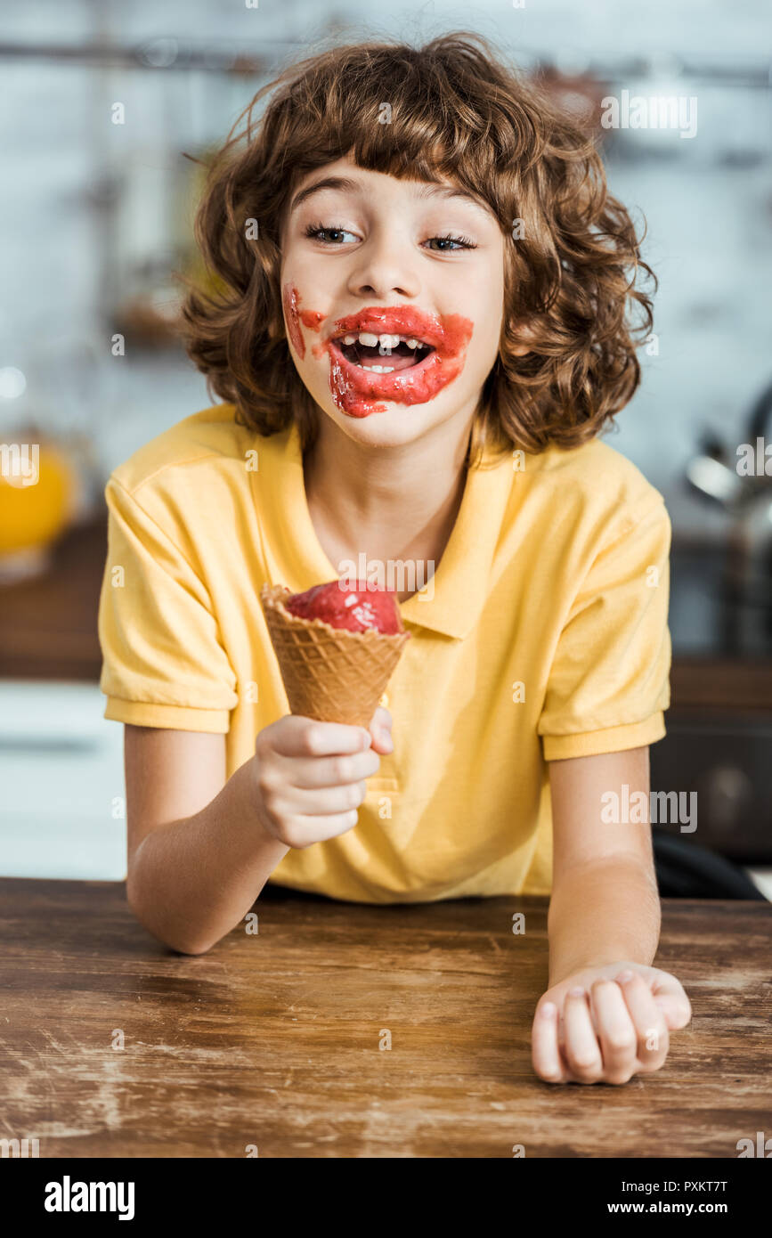Adorable happy boy avec de la glace sur le visage délicieux holding ice cream cone Banque D'Images