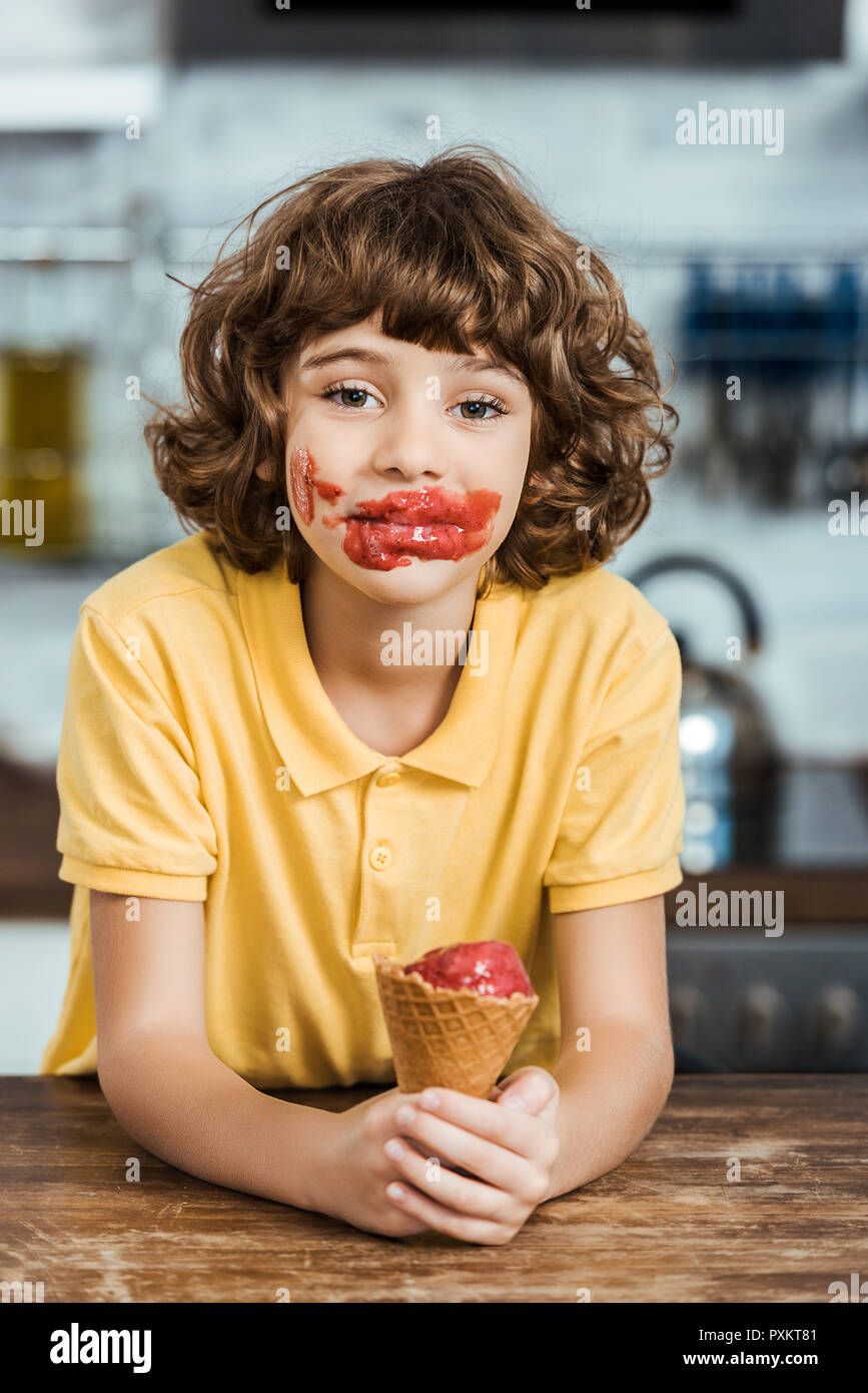 Adorable garçon avec de la glace sur le visage délicieux holding ice cream cone et looking at camera Banque D'Images