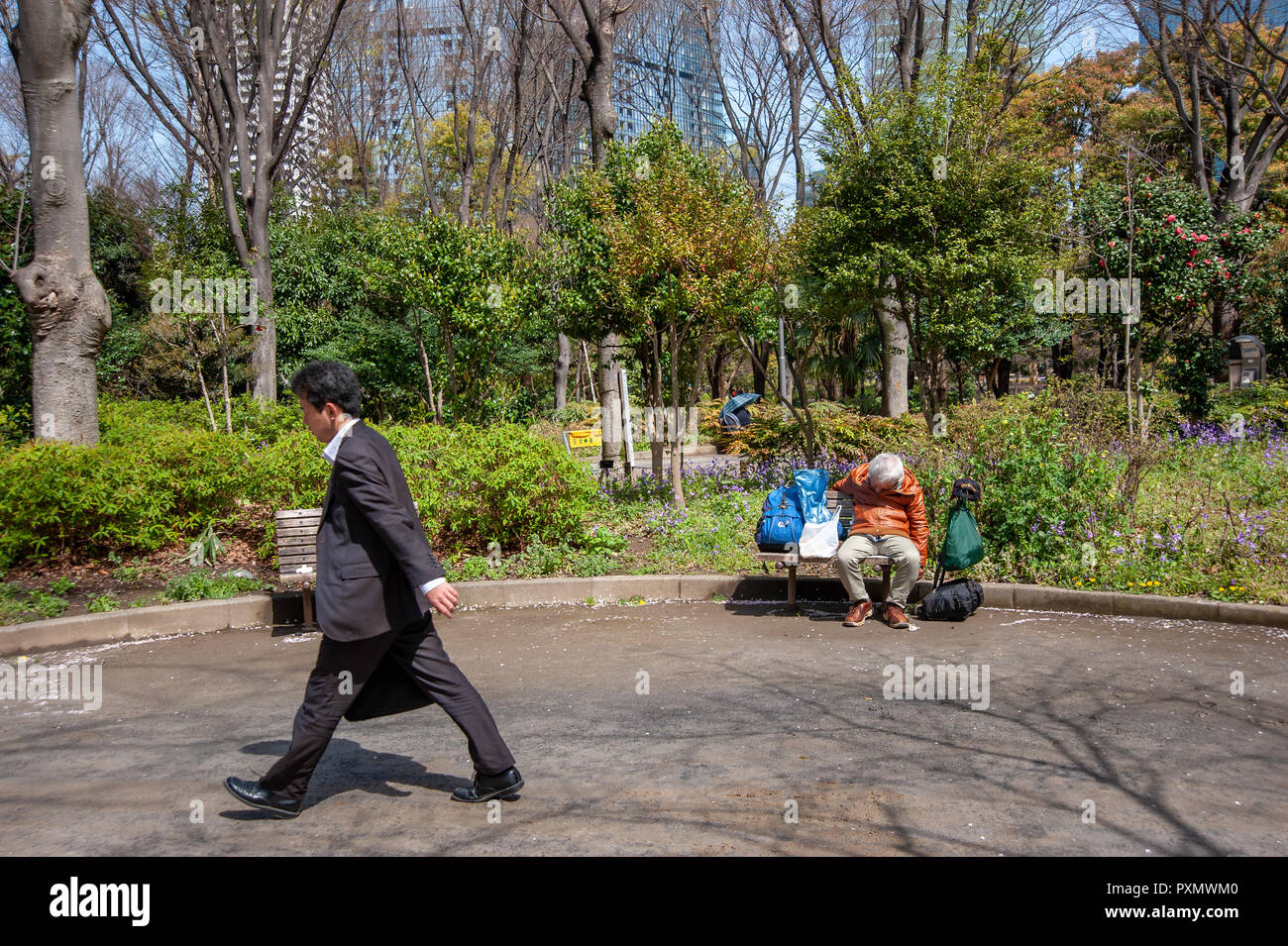 Businessman walking cours des sans-abri dormir sur un banc dans le parc Shinjuku Chuo, Tokyo, Japon Banque D'Images